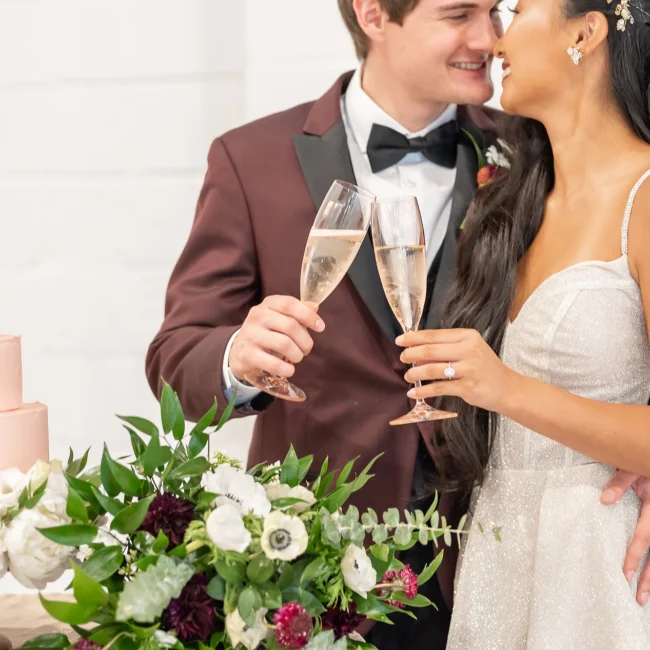 Bride and groom toasting with champagne beside the wedding cake and bouquet