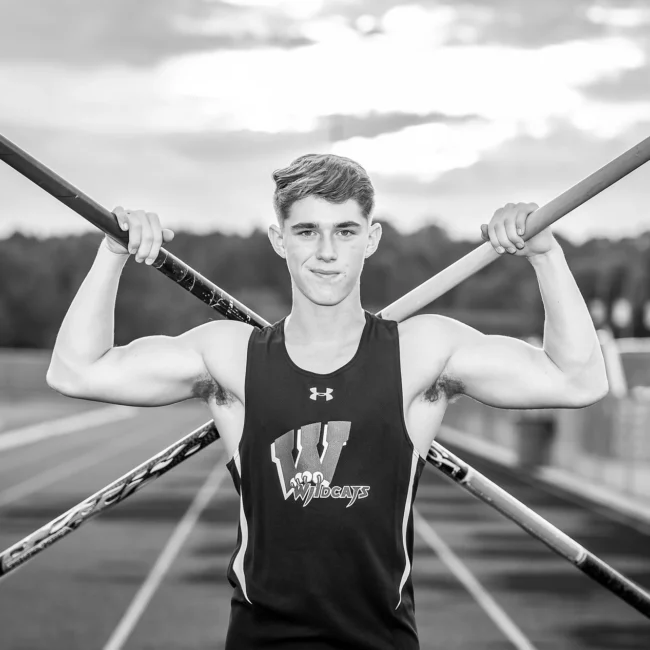 Black and white senior portrait of a track athlete holding vaulting poles on the track