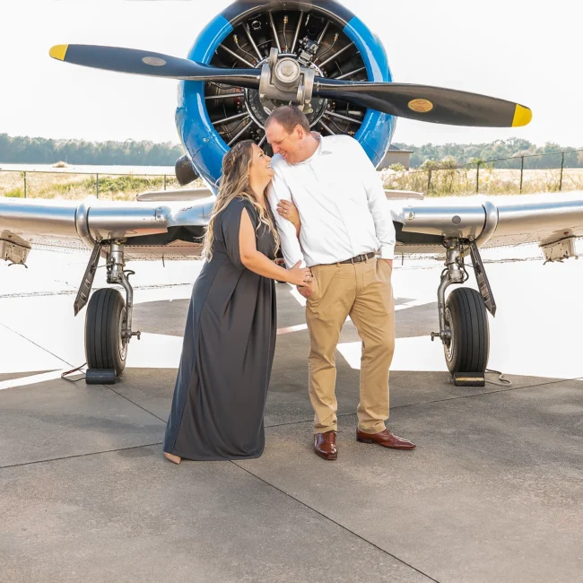 Couple embracing in front of a vintage propeller airplane