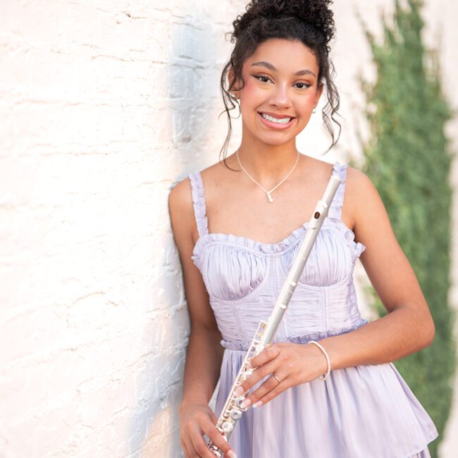 Senior girl in a lavender dress holding a flute against a white wall
