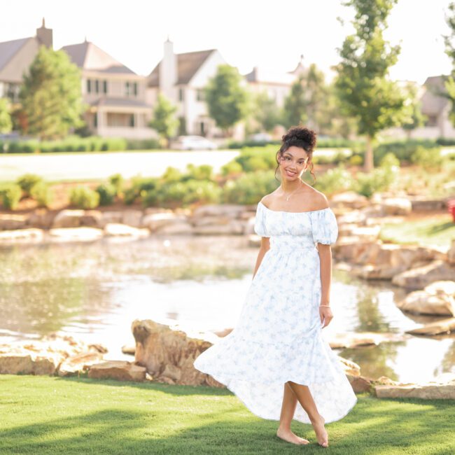 Senior girl in a white off-shoulder dress by a garden pond