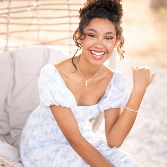 Senior girl in a floral dress smiling in a hanging wicker chair