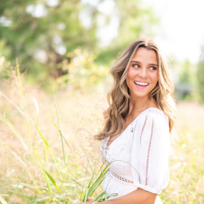 Smiling senior girl in a white dress among tall summer grass