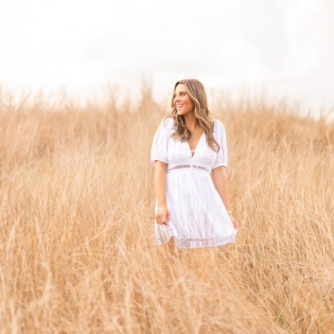 Senior girl in a white dress standing in a golden grass field
