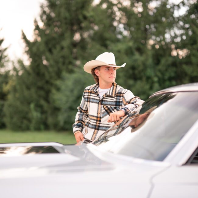 Senior guy in a cowboy hat leaning on a classic white car