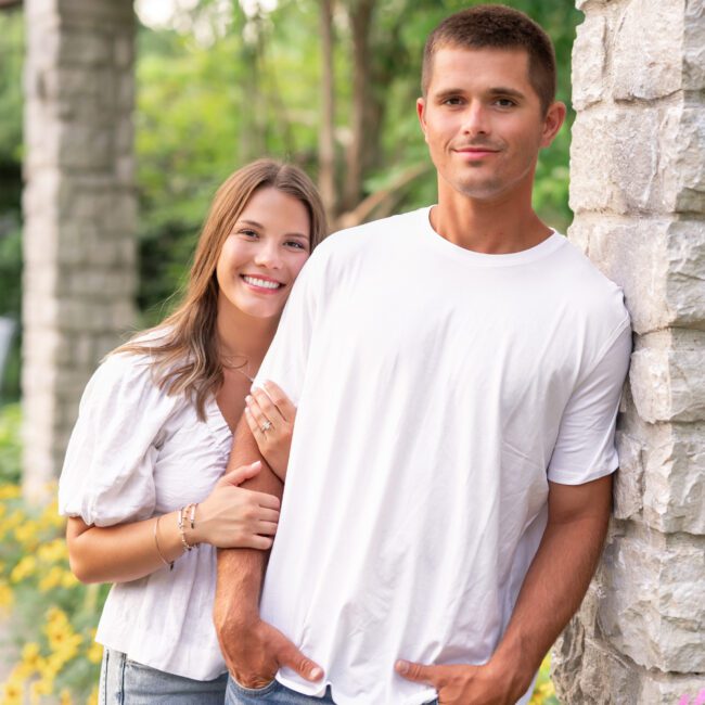 Couple standing arm in arm beside a stone pillar in a garden