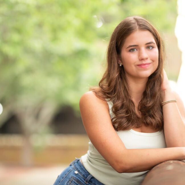 Senior girl in a white top sitting in a leafy park