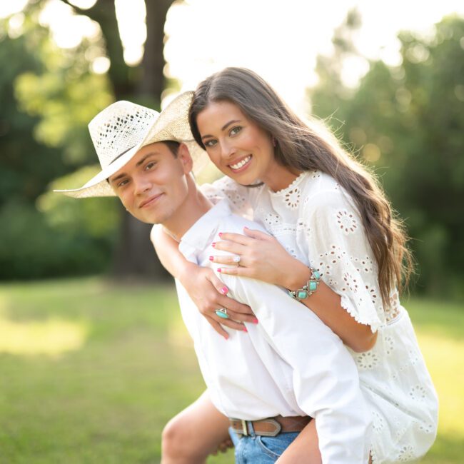 Couple laughing as she hugs him from behind in a grassy field