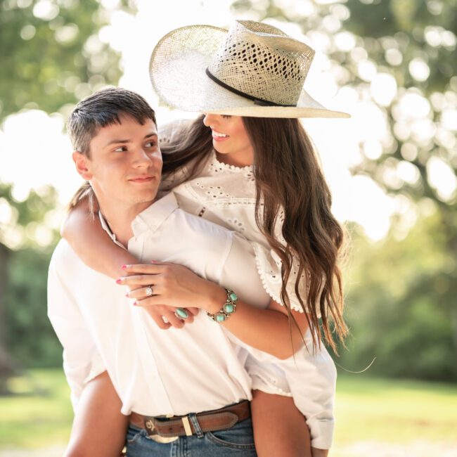 Man giving his fiancée a piggyback ride, her wearing his cowboy hat
