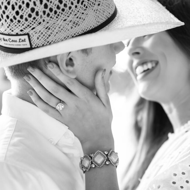 Black and white close-up of a couple in a cowboy hat about to kiss, showing her engagement ring