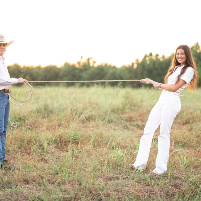 Man lassoing his fiancée with a rope in an open field