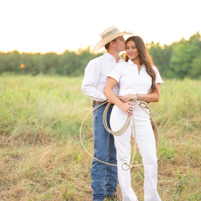 Couple holding each other with a lasso in a grassy field at sunset