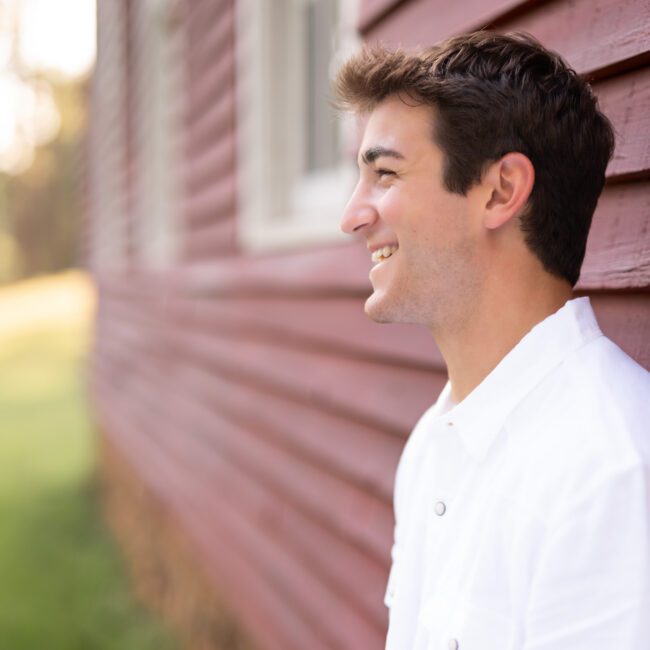 Senior guy in a white shirt smiling beside a red barn
