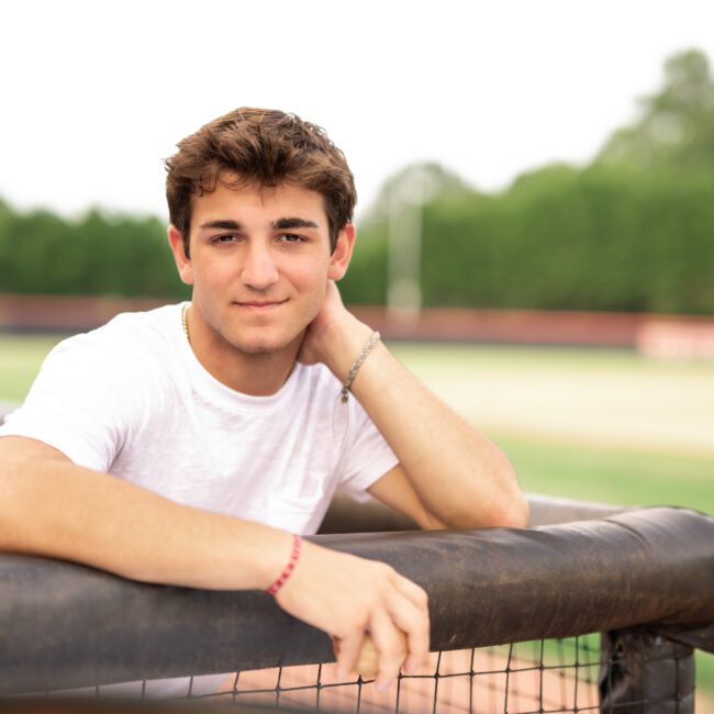 Senior guy resting his chin on a fence at the baseball field