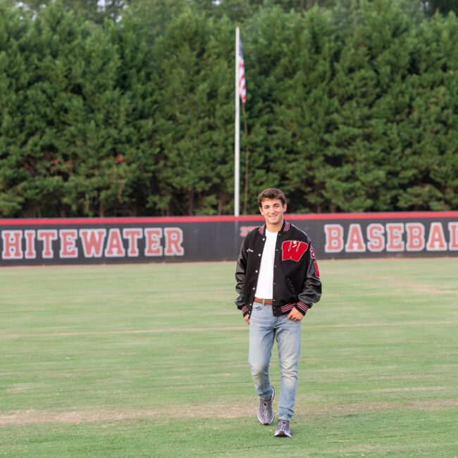 Senior guy in a letterman jacket walking across the baseball field