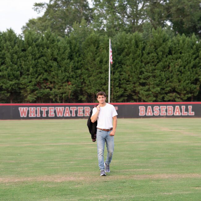 Senior guy walking across the baseball field holding his jacket