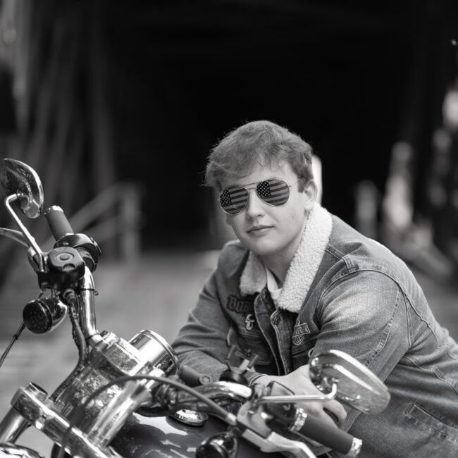 Black and white portrait of a senior guy in sunglasses on a motorcycle