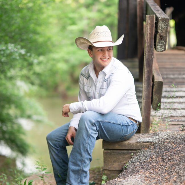 Senior guy in a cowboy hat sitting outside a wooden covered bridge