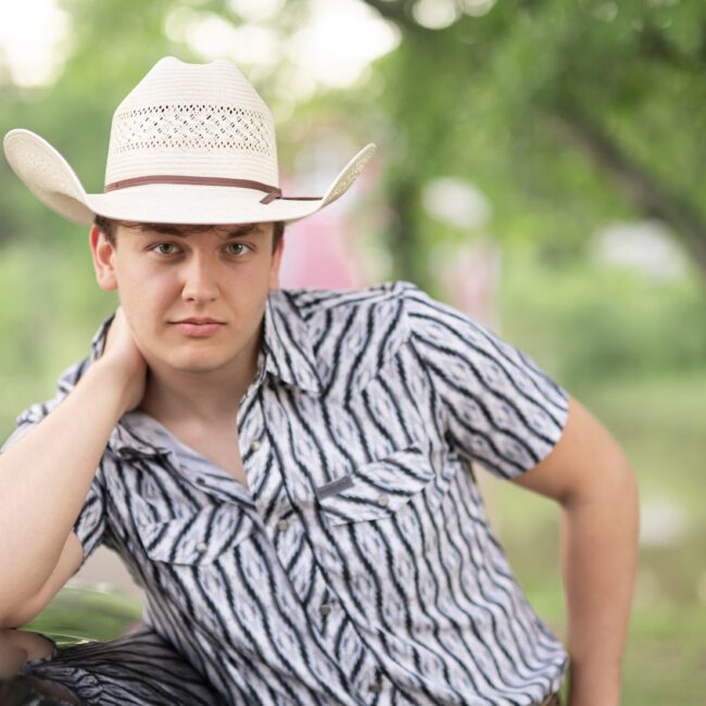 Senior guy in a cowboy hat and striped shirt posing by the water